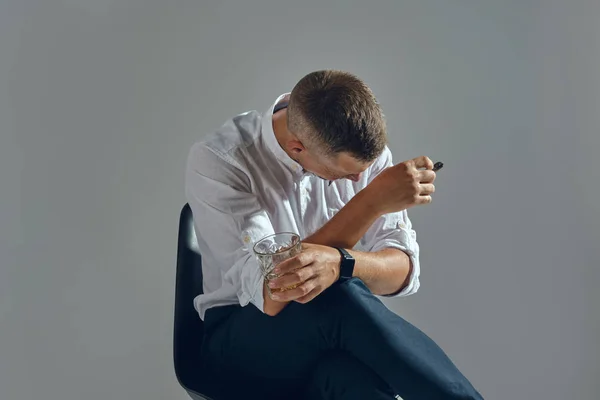 Mann mit stilvollem Schnurrbart, klassisch in weißem Hemd und dunkler Hose sitzt auf Stuhl und genießt Zigarre. Grauer Hintergrund, Nahaufnahme. — Stockfoto