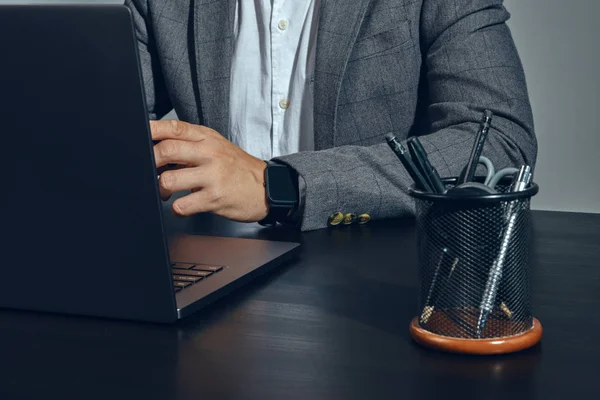 Handen van zakenman, gekleed in klassiek pak, wit shirt, poseren aan de tafel in het kantoor, werken op zijn laptop, grijze achtergrond. Close-up. — Stockfoto