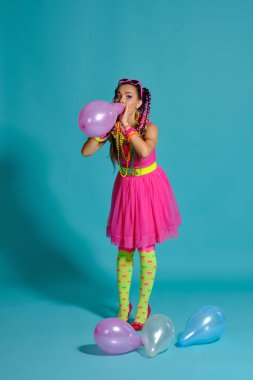Çok renkli saç stili ve parlak makyajlı güzel bir kız. Stüdyoda hava balonlarıyla mavi arka planda poz veriyor..
