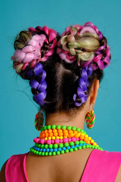 Belle fille aux cheveux en tresses multicolores et au maquillage éclatant, posant en studio sur fond bleu.. — Photo