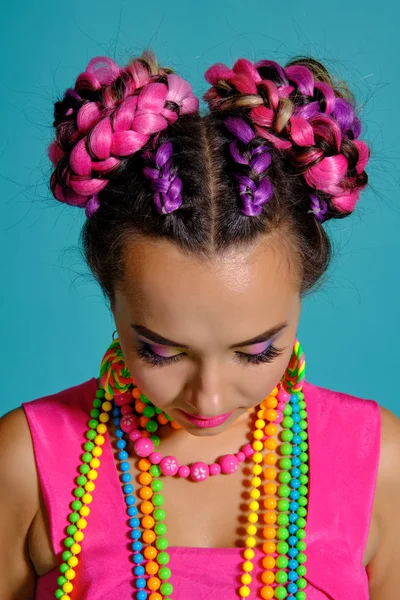 Schöne Mädchen mit mehrfarbigen Zöpfen Frisur und helles Make-up, posiert im Studio vor blauem Hintergrund. — Stockfoto