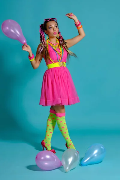 Preciosa chica con un estilo de pelo y maquillaje brillante de varios colores, posada en estudio con globos de aire sobre fondo azul.. —  Fotos de Stock