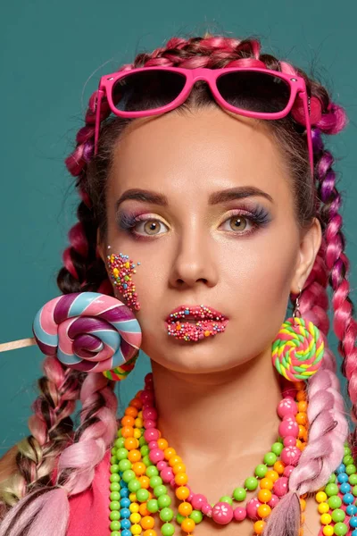 Härlig flicka med en flerfärgad flätor frisyr och ljusa make-up, poserar i studio mot en blå bakgrund, håller en klubba i handen. — Stockfoto