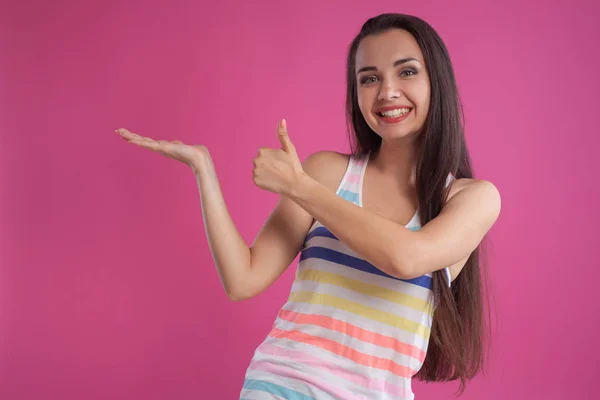 Brunette woman with long hair, dressed in colorful striped shirt, posing against pink studio background. Sincere emotions. Close-up. — Stock Photo, Image