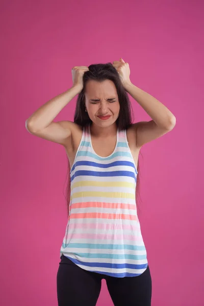 長い髪のブルネットの女性は、ピンクのスタジオの背景に対してポーズをカラフルな縞模様のシャツに身を包んだ。誠実な感情。閉鎖. — ストック写真