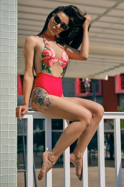 Retrato de una mujer descansando en un centro recreativo u hotel con piscina. Vestido con un colorido traje de baño y gafas de sol . — Foto de Stock