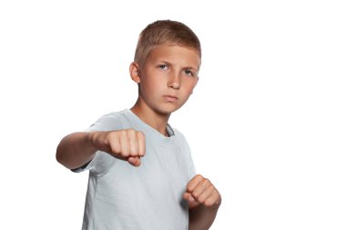 Beyaz tişörtlü yakışıklı sarışın bir gencin yakın plan portresi. Boks yapıyor ve beyaz stüdyo arka planında izole bir şekilde poz verirken kameraya bakıyor. Samimi duygular, mutlu çocukluk kavramı.