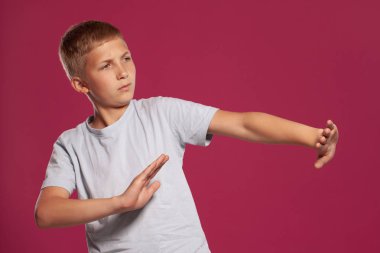 Beyaz tişörtlü yakışıklı sarışın bir gencin yakın plan portresi. Korkmuş görünüyor ve pembe stüdyo geçmişine karşı poz verirken kendini korumaya çalışıyor. Samimi duygular, mutlu çocukluk kavramı.