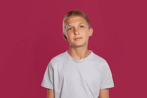 티셔츠를 금발의 소년의 클로즈업 분홍색 스튜디오 배경에 포즈를 취하면서 카메라를 — 스톡 사진