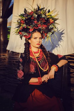 Esmer kız siyah ve kırmızı işlemeli Ukrayna otantik ulusal kostüm ve çiçek çelenk bir teras karşı poz olduğunu. Close.