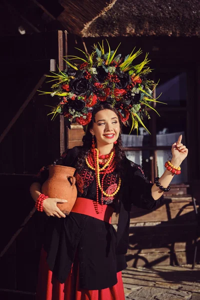 Brunette flicka i en svart och röd ukrainska broderade autentiska nationella kostym och en krans av blommor poserar stående vid grinden. — Stockfoto