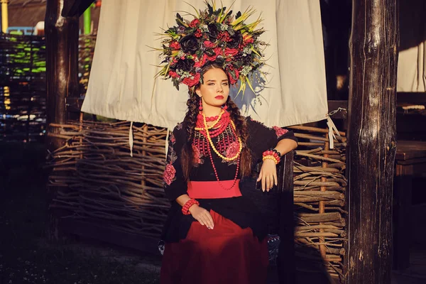 Barna lány egy fekete és piros hímzett ukrán hiteles nemzeti ruha és a koszorú virágok pózol ellen terasszal. Közeli. — Stock Fotó