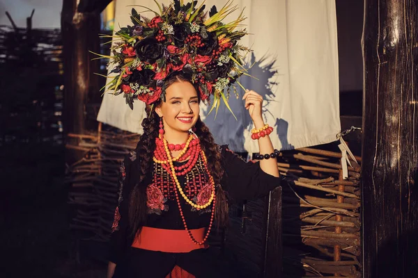 Bruna ragazza in un nero e rosso ricamato ucraino autentico costume nazionale e una corona di fiori è in posa contro una terrazza. Primo piano . — Foto Stock