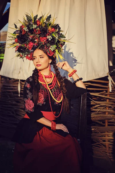 Brunette flicka i en svart och röd broderade ukrainska autentiska nationella kostym och en krans av blommor poserar mot en terrass. Närbild. — Stockfoto