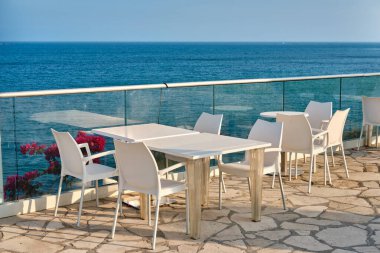 Beyaz masalı ve sandalyeli bir otelin restoran terası. Deniz kıyısı, Kalymnos adasında beyaz taş pelerin ya da Kıbrıs 'ta vali plajı.
