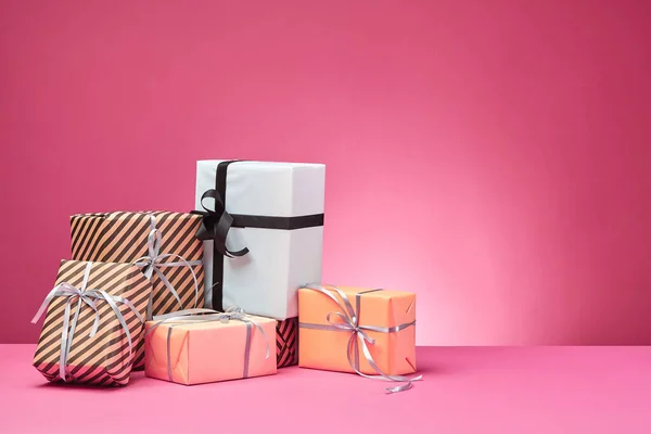 Diferentes tamaños, coloridas, rayas y lisas cajas de regalo de papel atadas con cintas y arcos sobre una superficie y fondo rosados. Cierre y copia del espacio. —  Fotos de Stock