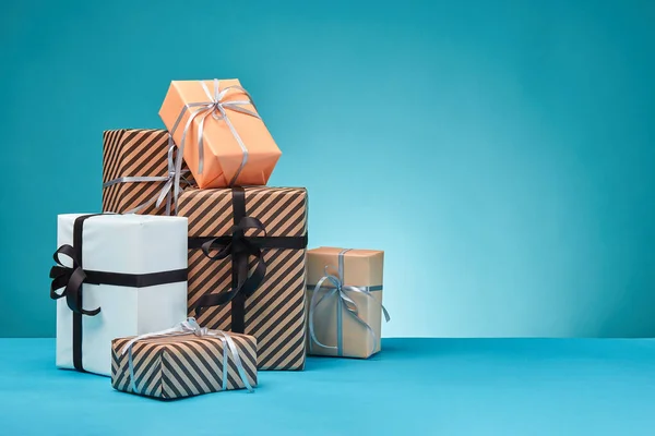 Diferentes tamaños, coloridas, rayas y lisas cajas de regalo de papel atadas con cintas y arcos sobre una superficie y fondo azules. Cierre y copia del espacio. — Foto de Stock