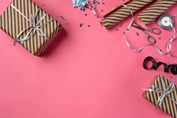 Diferentes tamaños, cajas de regalo rayas y marrones unidas con cintas negras y plateadas y arcos en un fondo rosado. Cierre, espacio de copia, vista superior. —  Fotos de Stock