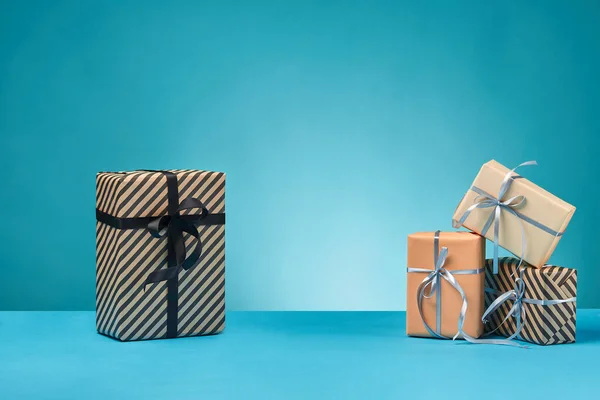 Diferentes tamaños, coloridas, rayas y lisas cajas de regalo de papel atadas con cintas y arcos sobre una superficie y fondo azules. Cierre y copia del espacio. —  Fotos de Stock