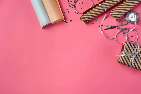 Boîte-cadeau brun rayé nouée avec un ruban argenté sur fond rose. Du papier d'emballage et des ciseaux se trouvent à proximité. Gros plan, espace de copie, vue de dessus. — Photo
