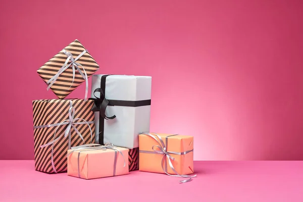 Diferentes tamaños, coloridas, rayas y lisas cajas de regalo de papel atadas con cintas y arcos sobre una superficie y fondo rosados. Cierre y copia del espacio. — Foto de Stock