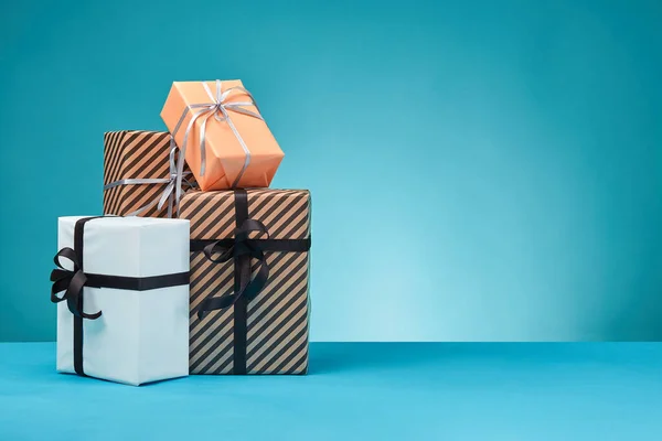 Boîtes cadeaux de différentes tailles, colorées, rayées et en papier ordinaire, attachées avec des rubans et des arcs sur une surface et un fond bleus. Gros plan, espace de reproduction. — Photo