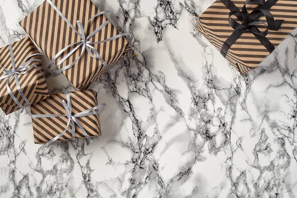 Different sizes, striped, brown, paper gift boxes tied with black and silver ribbons and bows on a marble background. Close-up, copy space, top view.