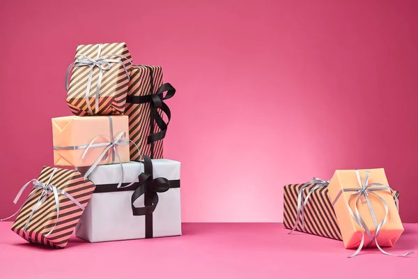 Diferentes tamaños, coloridas, rayas y lisas cajas de regalo de papel atadas con cintas y arcos sobre una superficie y fondo rosados. Cierre y copia del espacio. —  Fotos de Stock