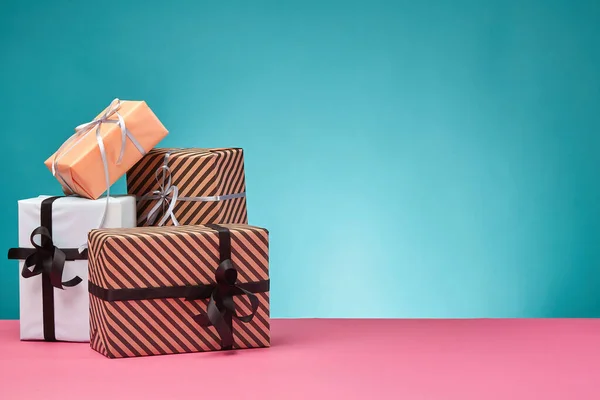 Diferentes tamaños, coloridas, rayas y lisas cajas de regalo de papel atadas con cintas y arcos en una superficie rosada y fondo azul. Cierre y copia del espacio. —  Fotos de Stock