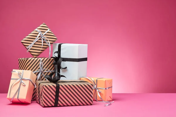 Different sizes, colorful, striped and plain paper gift boxes tied with ribbons and bows on a pink surface and background. Close-up, copy space. — Stock Photo, Image