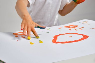 Beyaz tişörtlü küçük sanatçı masasında hangi adam ve renkli resimlerle duruyor, elleriyle boyuyor. Beyazda izole edilmiş. Yakın plan..