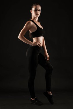 Siyah taytlı esmer kadın, üst ve spor ayakkabılı siyah arka planda poz veriyor. Fitness, spor salonu, sağlıklı yaşam tarzı konsepti. Tam uzunluk.