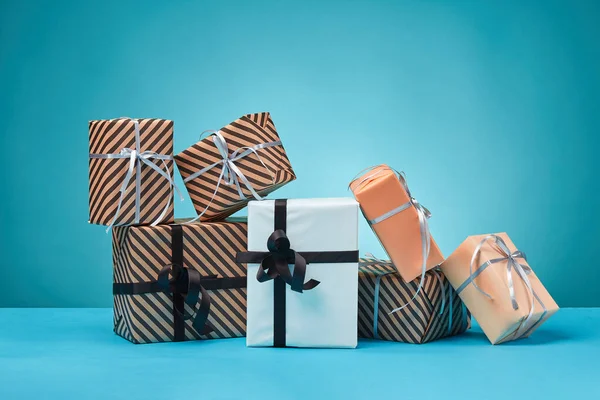 Diferentes tamaños, coloridas, rayas y lisas cajas de regalo de papel atadas con cintas y arcos sobre una superficie y fondo azules. Cierre y copia del espacio. —  Fotos de Stock