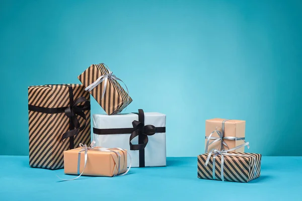 Diferentes tamaños, coloridas, rayas y lisas cajas de regalo de papel atadas con cintas y arcos sobre una superficie y fondo azules. Cierre y copia del espacio. —  Fotos de Stock