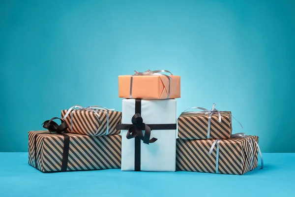 Diferentes tamaños, coloridas, rayas y lisas cajas de regalo de papel atadas con cintas y arcos sobre una superficie y fondo azules. Cierre y copia del espacio. — Foto de Stock