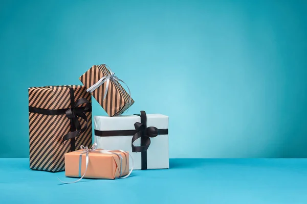 Diferentes tamaños, coloridas, rayas y lisas cajas de regalo de papel atadas con cintas y arcos sobre una superficie y fondo azules. Cierre y copia del espacio. —  Fotos de Stock