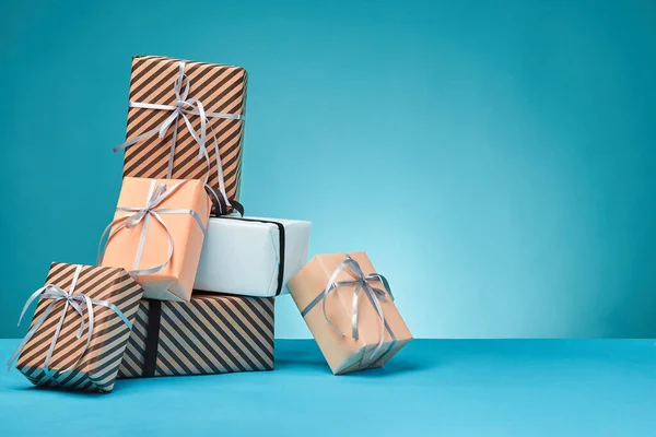 Diferentes tamaños, coloridas, rayas y lisas cajas de regalo de papel atadas con cintas y arcos sobre una superficie y fondo azules. Cierre y copia del espacio. —  Fotos de Stock