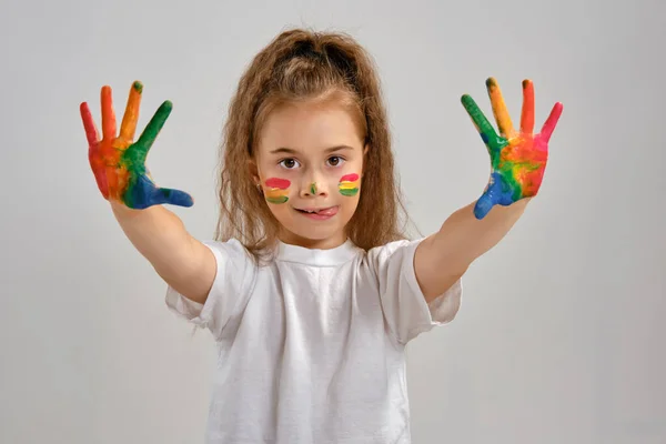 Little girl in white t-shirt is posing standing isolated on white and showing her painted hands, face. Art studio. Close-up.