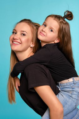 Siyah gömlek ve kot pantolon giymiş komik saç stilleri olan anne ve kızı mavi bir stüdyo geçmişine karşı poz veriyorlar. Yakın çekim..