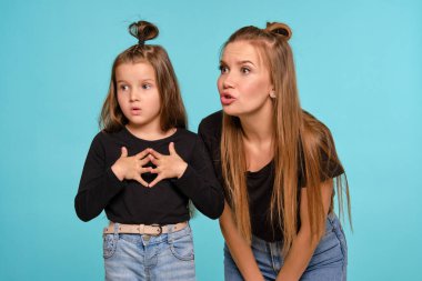 Siyah gömlek ve kot pantolon giymiş komik saç stilleri olan anne ve kızı mavi bir stüdyo geçmişine karşı poz veriyorlar. Yakın çekim..