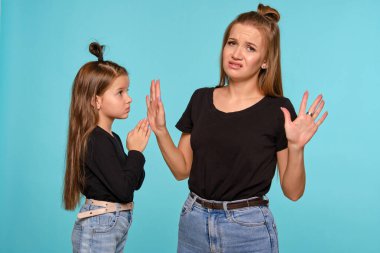 Siyah gömlek ve kot pantolon giymiş komik saç stilleri olan anne ve kızı mavi bir stüdyo geçmişine karşı poz veriyorlar. Yakın çekim..