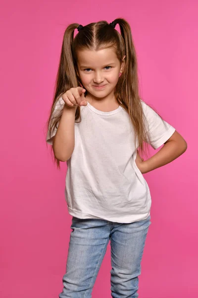 Pequeña chica con colas, vestida de camiseta blanca y vaqueros azules está posando sobre un fondo de estudio rosa. Cerrado el tiro. Emociones sinceras. —  Fotos de Stock