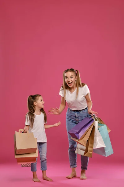 Mamá e hija con colas, vestida de camisetas blancas y vaqueros azules se ponen sobre fondo rosado con paquetes en las manos. Larga duración. — Foto de Stock