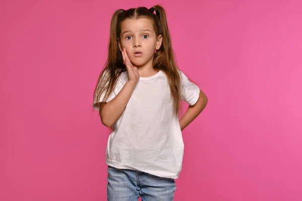 Девочка с пончиками, одетая в белую футболку и синие джинсы, позирует на розовом студийном фоне. Выстрел в упор. Искренние эмоции. — стоковое фото