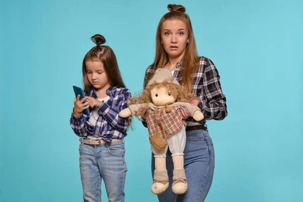 Mutter und Tochter in karierten Hemden und blauen Jeans nutzen das Smartphone, während sie vor blauem Studiohintergrund posieren. Nahaufnahme. — Stockfoto