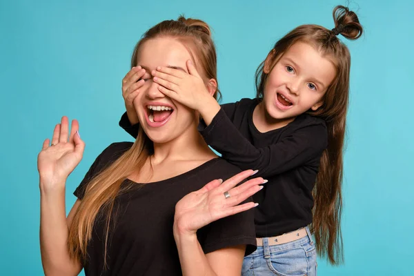 Mutter und Tochter mit lustigen Frisuren posieren in schwarzen Hemden und blauen Jeans vor blauem Studiohintergrund. Nahaufnahme. — Stockfoto