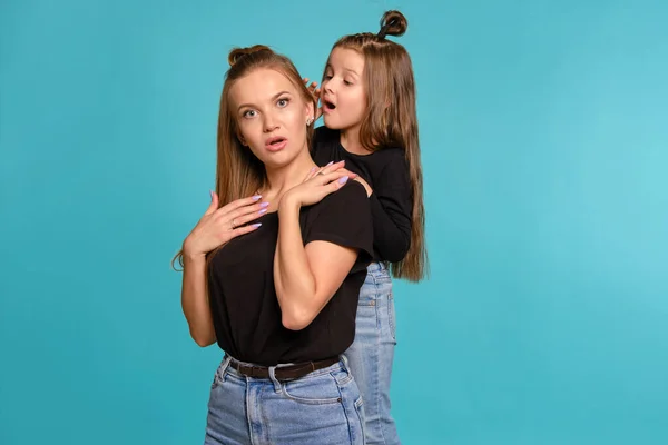 Máma a dcera s legračními účesy, oblečené v černých košilích a džínách modré džíny pózují na pozadí modrého studia. Detailní záběr. — Stock fotografie