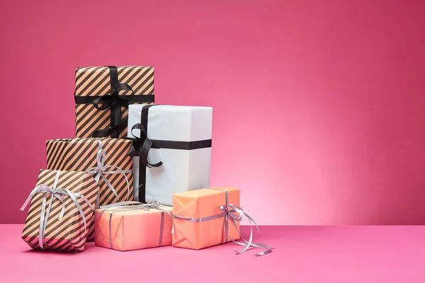 Diferentes tamaños, coloridas, rayas y lisas cajas de regalo de papel atadas con cintas y arcos sobre una superficie y fondo rosados. Cierre y copia del espacio. —  Fotos de Stock