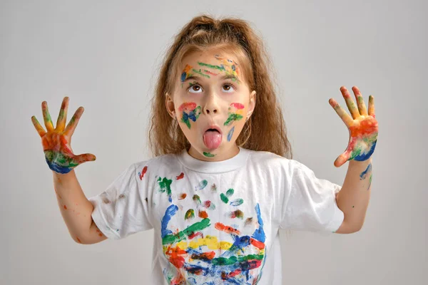 Little girl in white t-shirt is posing standing isolated on white and gesticulating with her painted in different colors palms. Art studio. Close-up. — Stock Photo, Image