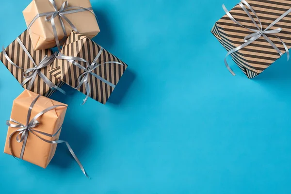 Colorful, striped and plain, brown and pink paper gift boxes tied with silver ribbons and bows on a blue background. Close-up, copy space, top view.